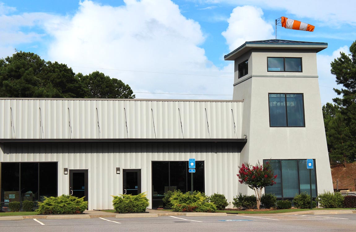The outside of the Aventure Aviation warehouse, with a windsock visible from the top of a tower portion of the building