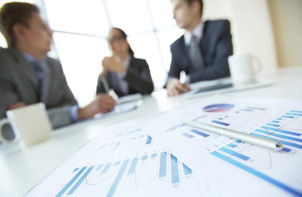Three business person, out of focus, at a conference table in front of statistical charts
