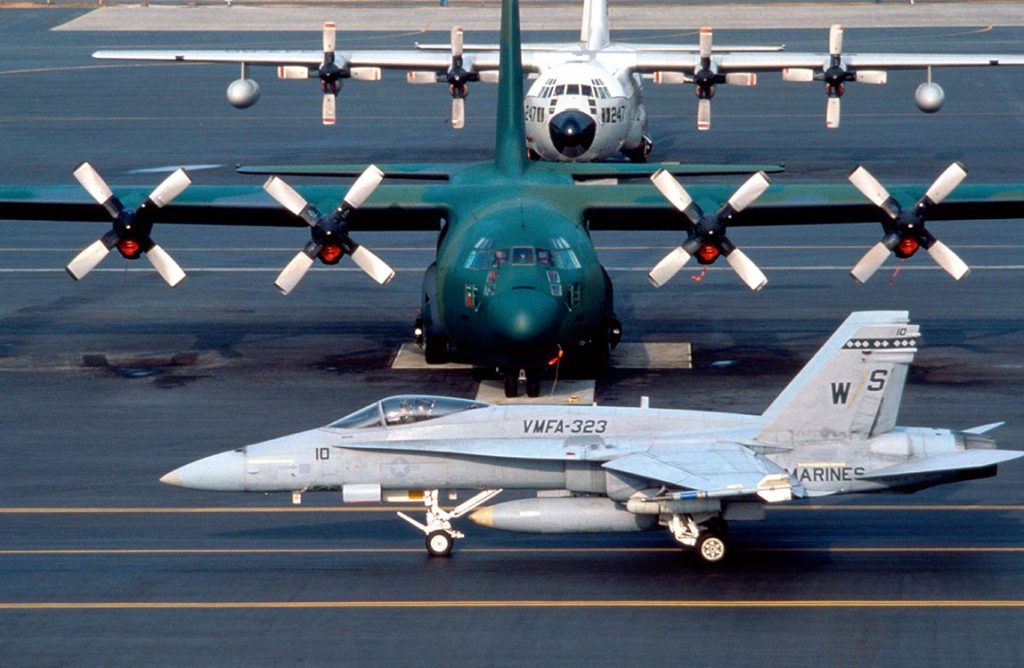 A military jet aircraft and two military cargo airplanes on the tarmac