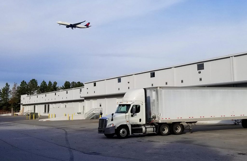 Exterior of Aventure's new warehouse loading dock and truck; airplane taking off in background