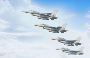 Four F-16 fighter jets flying in close formation in front of a blue sky