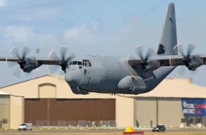 C-130 Hercules aircraft landing in front of a hanger
