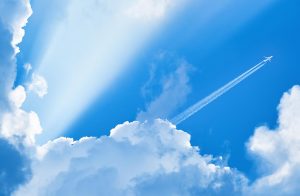 Airplane with contrails in the distance with a bright blue sky and huge clouds