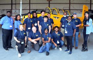 15 aviation students and staff pose in front of a vintage yellow fighter plane at the Commemorative Air Force Airbase Georgia Museum