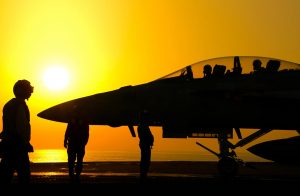 F-18 Hornet fighter jet on deck of aircraft carrier in sillouette against bright sun and yello sky