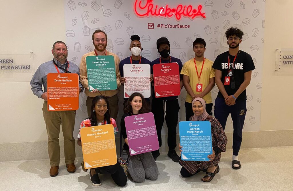 Nine Aventure Aviation employees in two rows, holding up large signs representing the packaging of Chick-fil-A dipping sauces