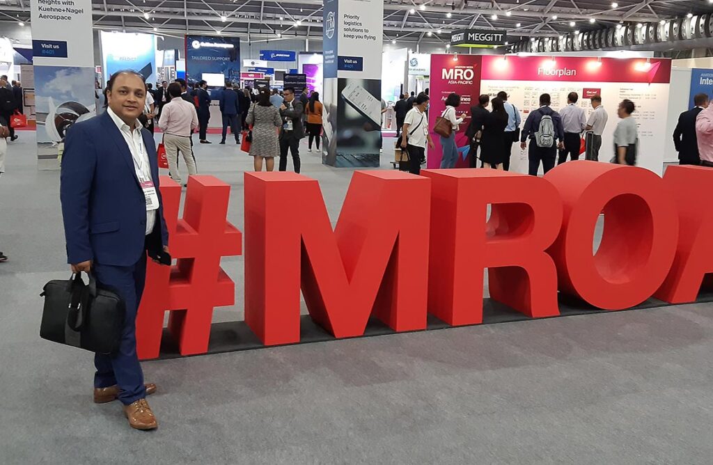 Aventure Aviation's Saurabh Tripathi in front of huge 3D letters on the floor saying "#MRO" with several conference booths in background