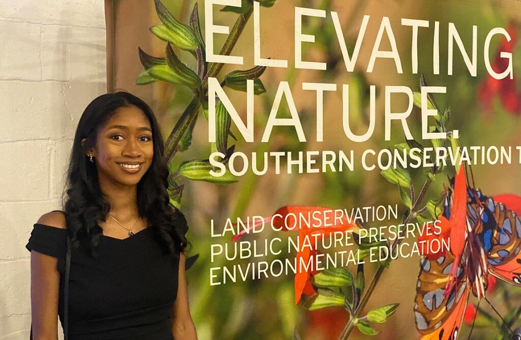 Aventure Aviation office manager Chelsea Griffin poses in front of a banner saying "Elevating Nature" at the Southern Conservation Trust Gala