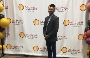A man poses in front of a backdrop saying "Midwest Food Bank Georgia" next to balloons