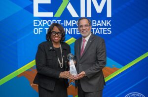 A woman presents an award to a man in front of a backdrop that says EXIM Export-Import Bank of the United States