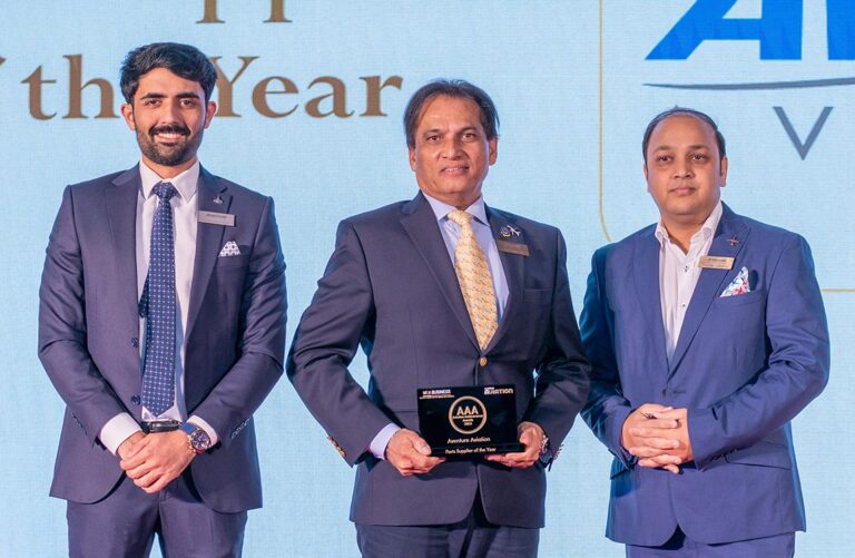 Three men in business suits smile for the camera, while the one in the middle holds an award plaque