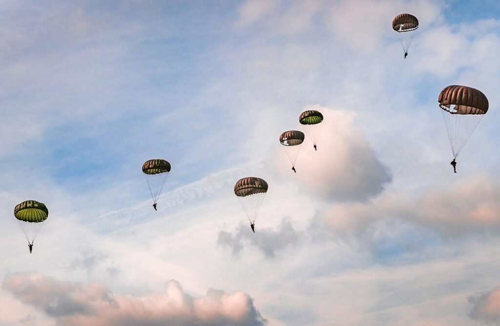 Several paratroopers glide with chutes open through a cloudy sky
