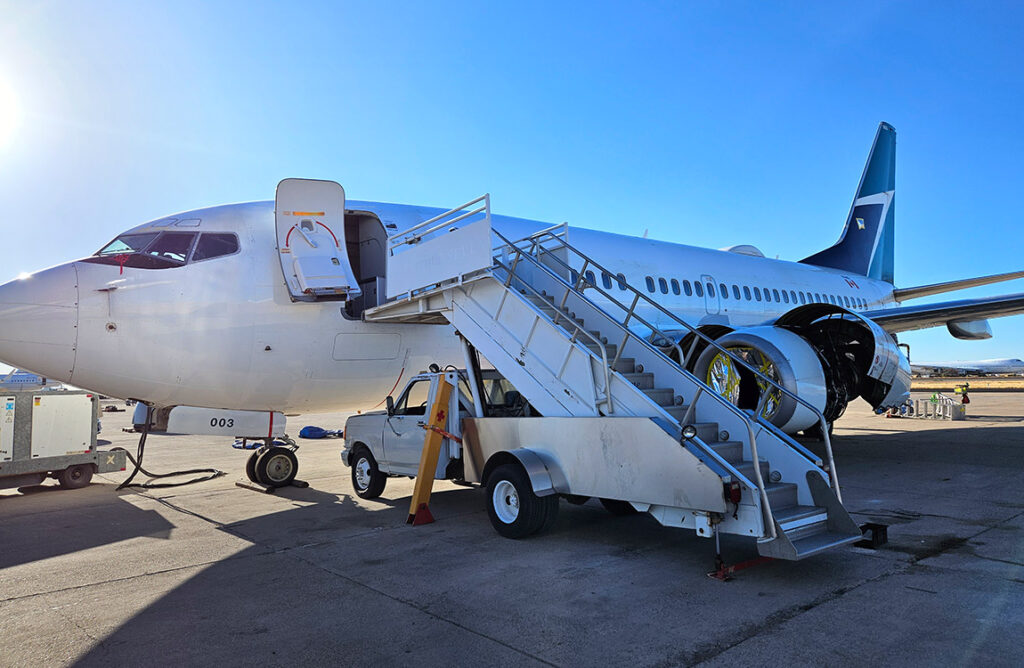 A jet aircraft with the logo of WestJet Airlines on the tail on the tarmac, with a truck with stairs on top leading to the front of the plane