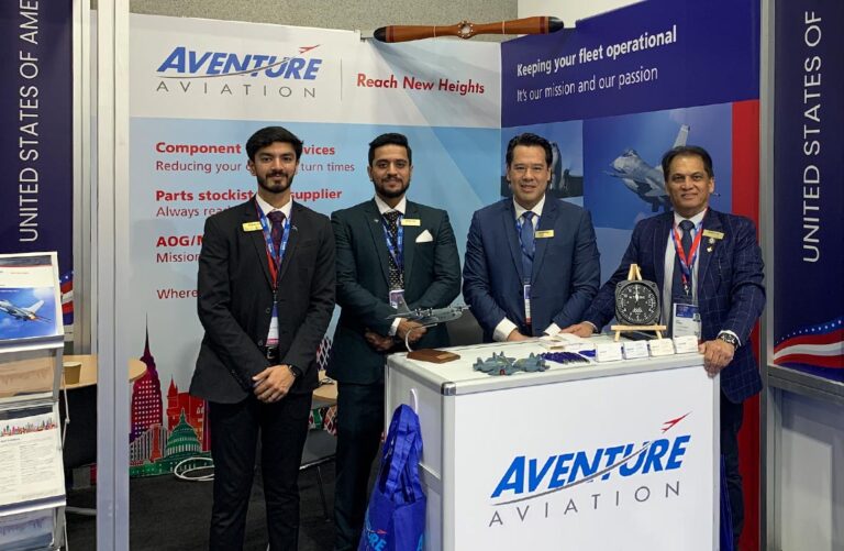 Four men in suits stand inside a tradeshow booth below a sign that says "Aventure Aviation – Reach New Heights"