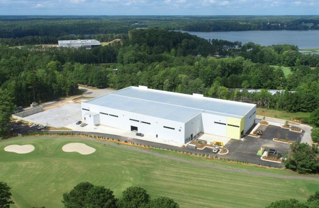 Huge warehouse and office building nearly completed next to a golf course with a lake in the background