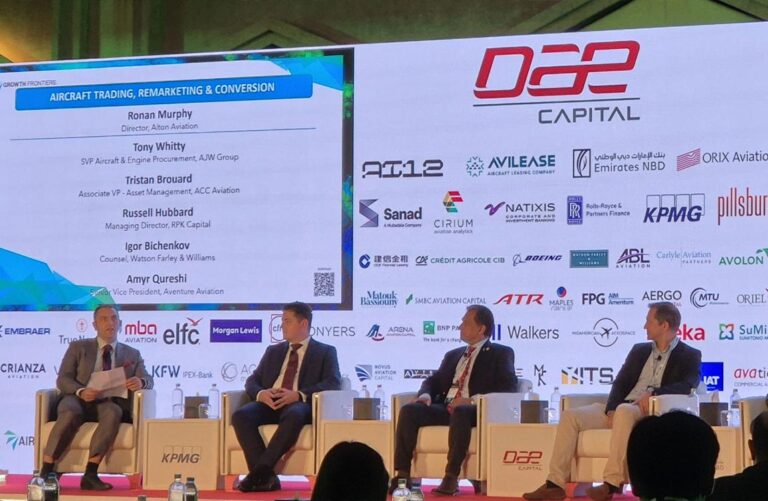 Four men on a large stage with a huge background full of corporate logos