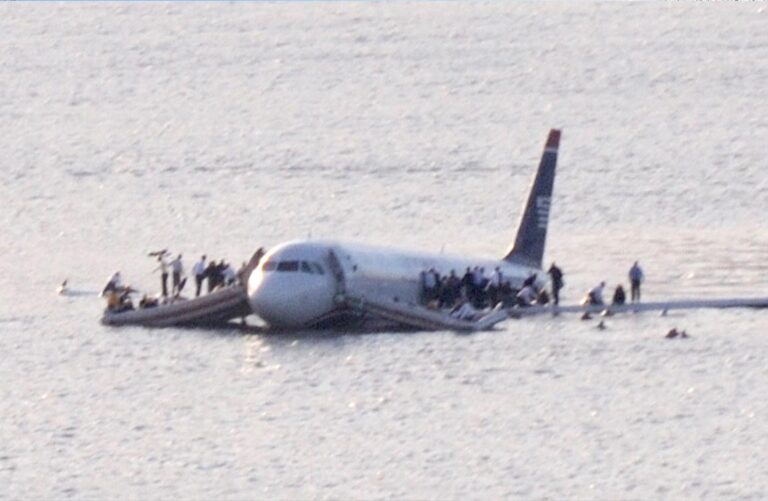 A commercial aircraft floats on a body of water, with people standing on its wings and evacuation slides