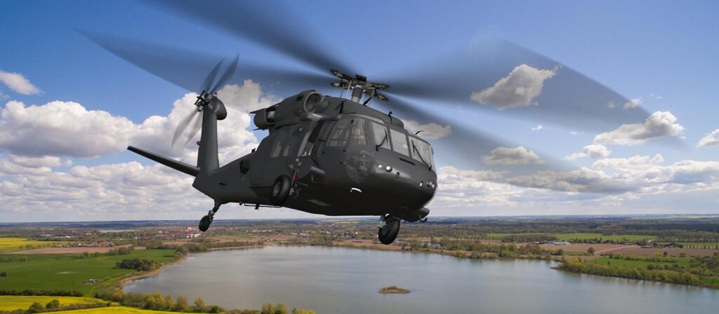 Close up aerial view of a Black Hawk military helicopter in flight over a large lake under a blue sky