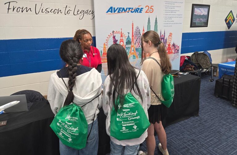 Three young students speak with an adult at a trade show