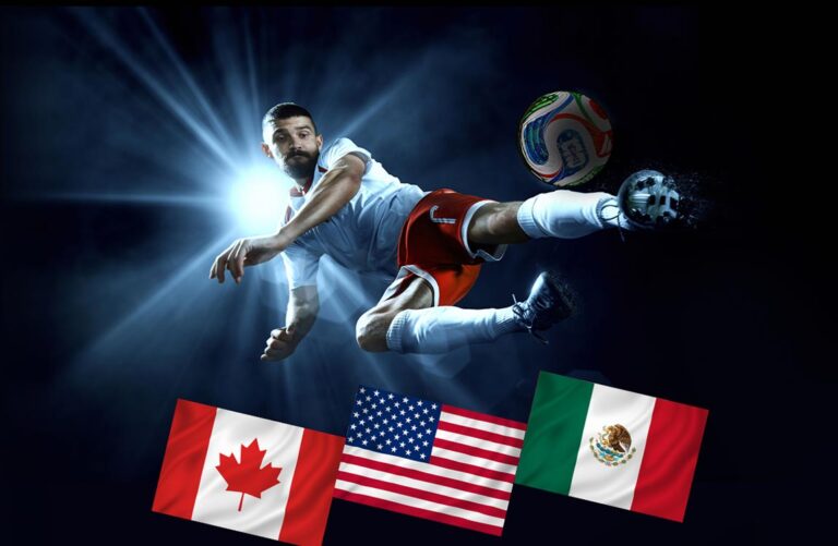 A soccer player in a stadium at night in front of a spotlight, kicks a ball in the air above the flags of Canada, USA, and Mexico