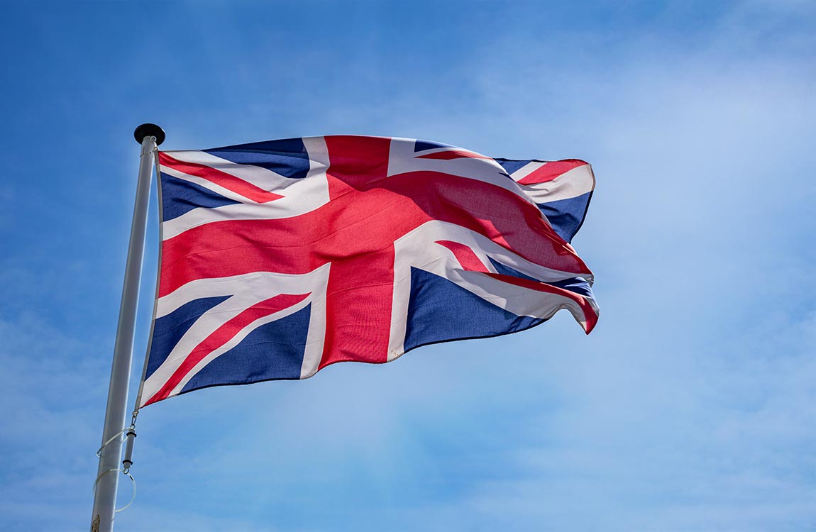 A British flag on a pole flies in the sky