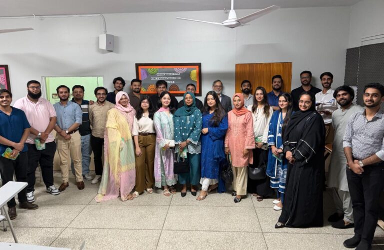A room of 25 men and women pose for a photo in a large room inside a place of business