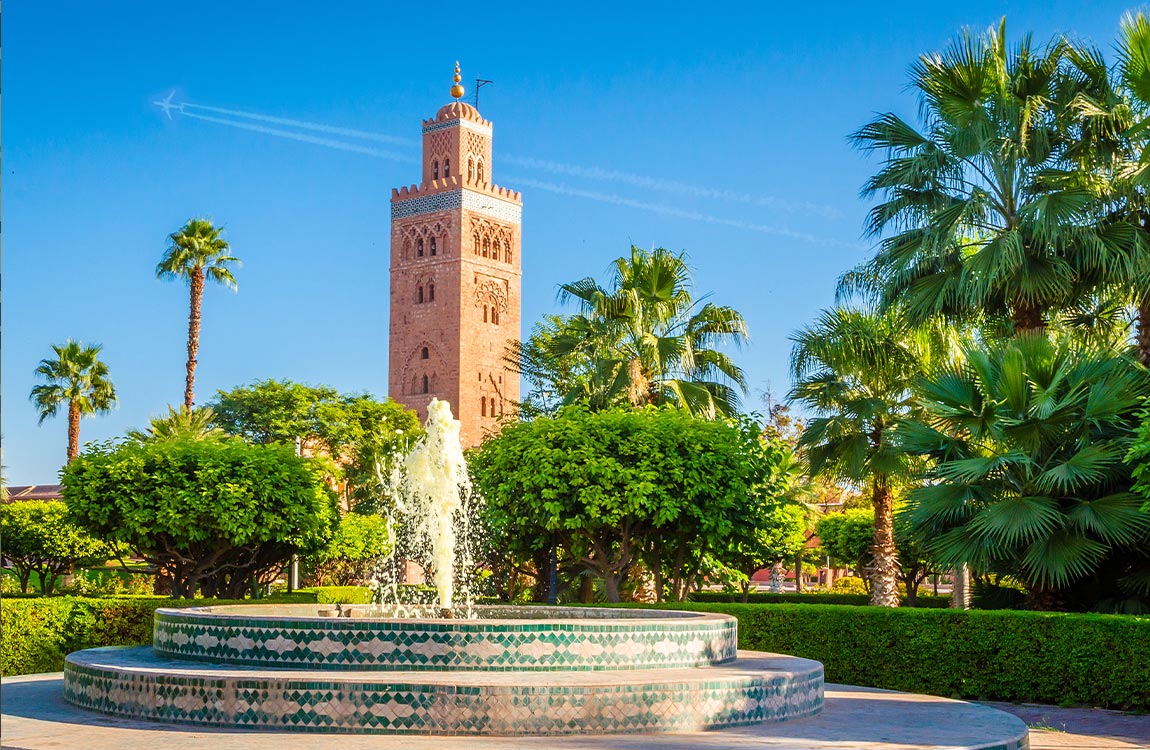 A minaret of the Koutoubia Mosque in Marrakesh, Morocco, surrounded by palm trees in front of a fountain